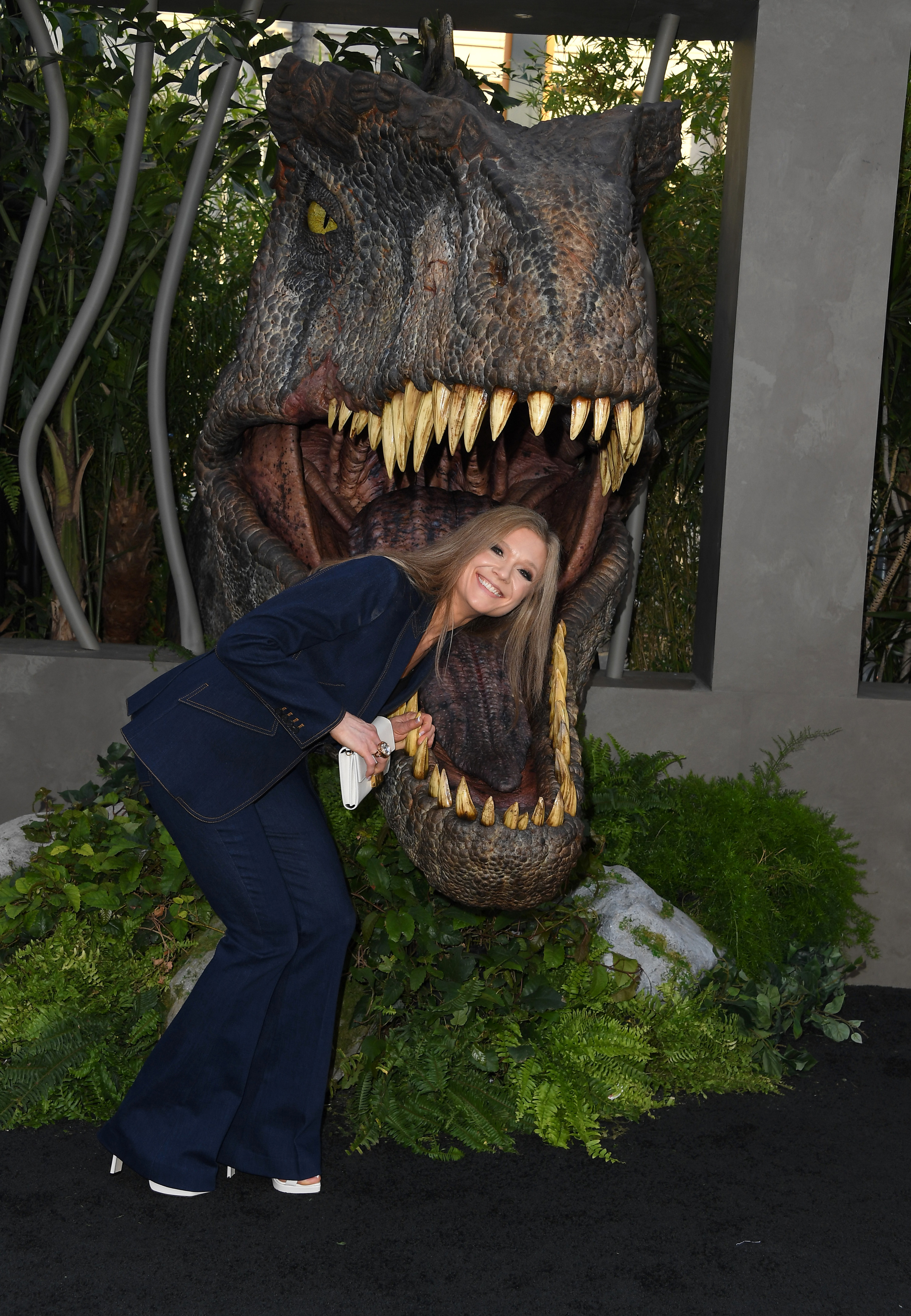 A grown Ariana smiling with her head inside the mouth of a giant dinosaur