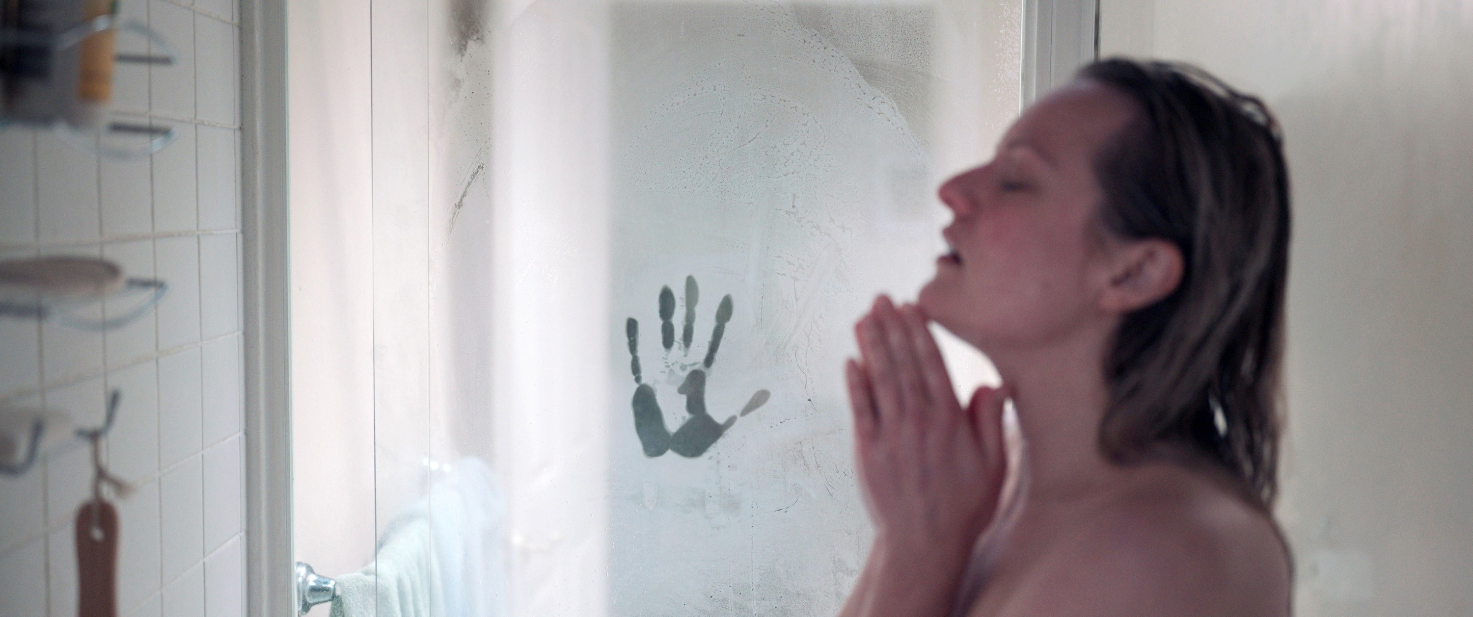 A woman in a shower with a mysterious handprint on the glass behind her