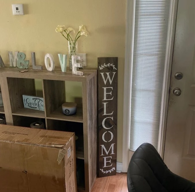A reviewer&#x27;s image of a wood welcome sign with coat and paint distressing