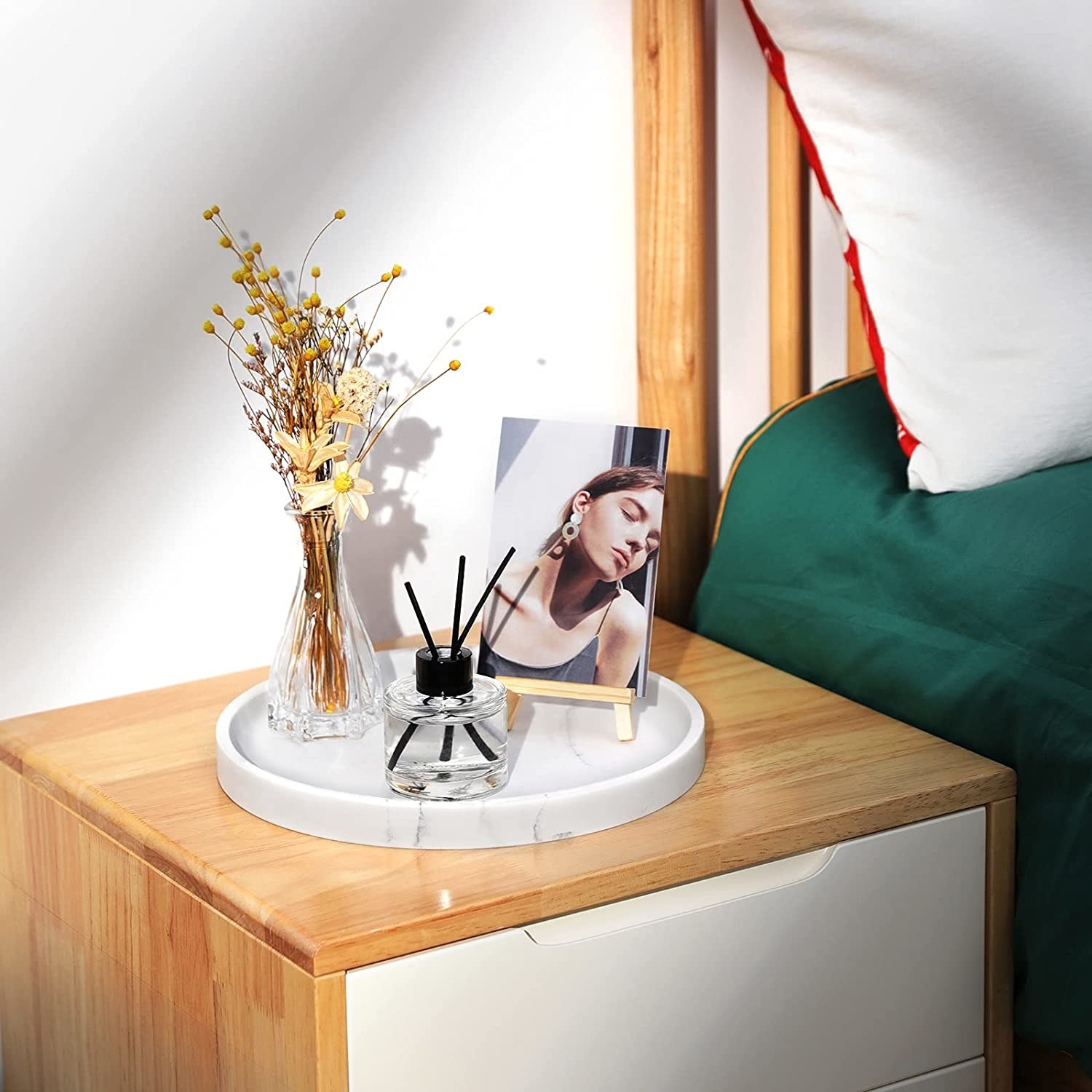 The tray with flowers, a picture, and a diffuser on it on a bedside table