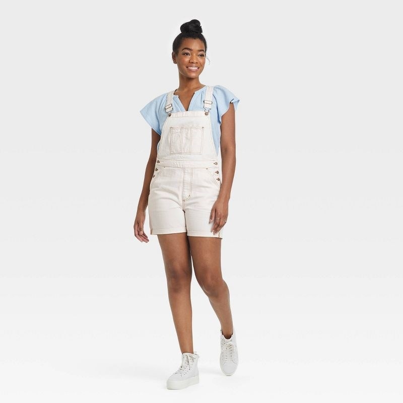 Model wearing white overall with blue tee and white sneakers