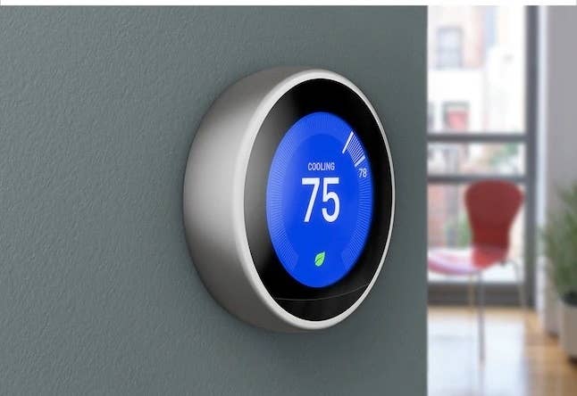 a smart thermostat in black attached to a green wall