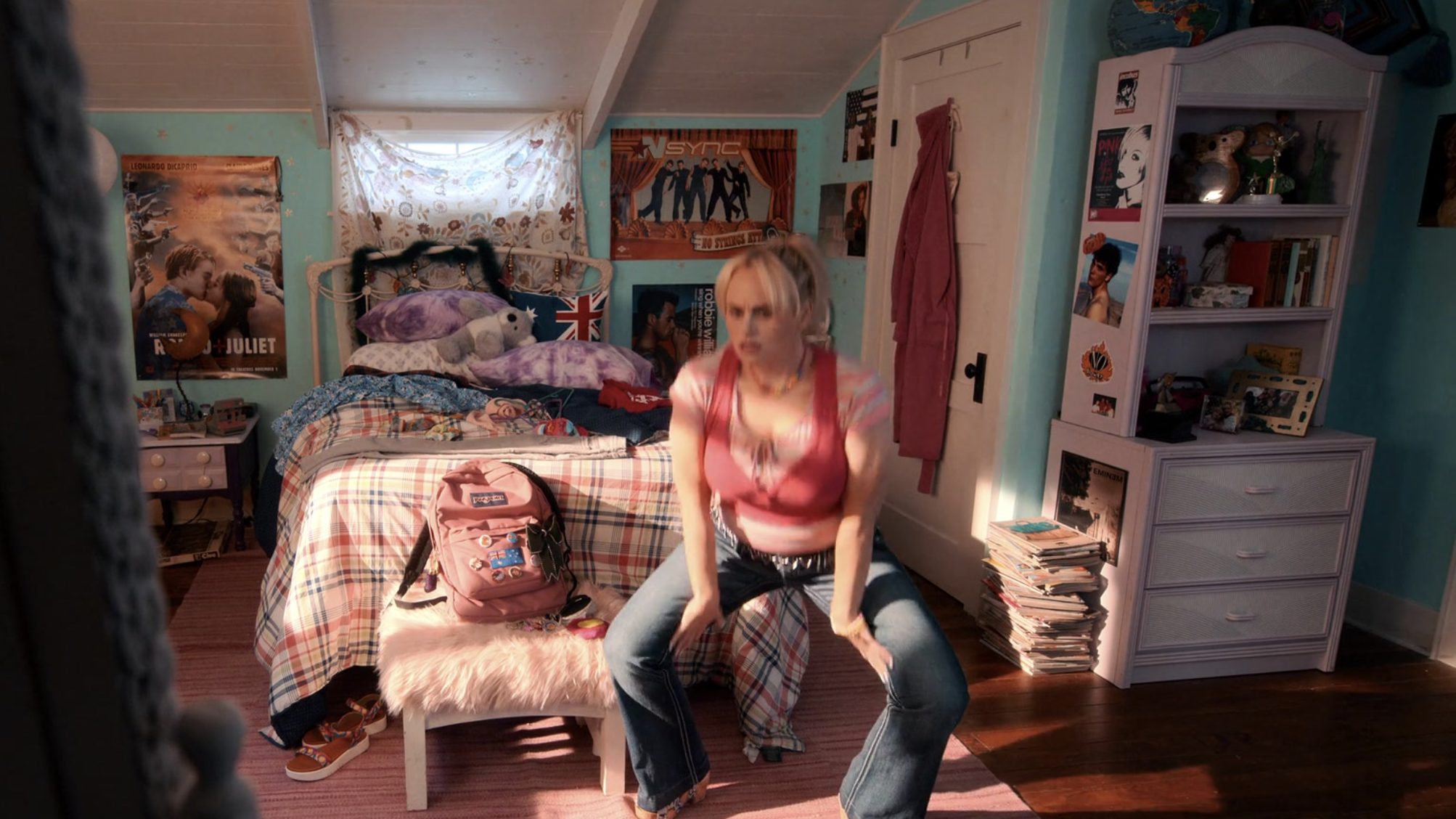 Rebel as Stephanie sitting on her bed with posters on her bedroom wall