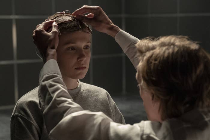 Eleven with a shaved head having cords attached to her head