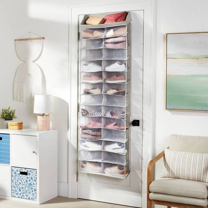 The grey and clear shoe storage rack hung over door and filled with pairs of shoes