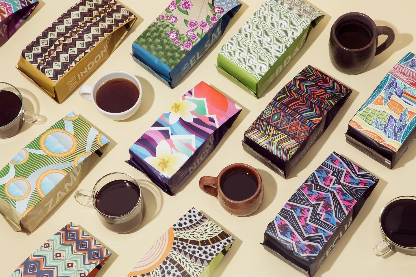 colorful bags of ground and whole bean coffee next to mugs filled with brewed coffee