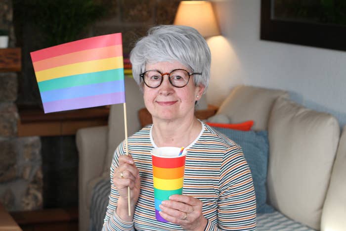 An older woman holding a cup and small flag both adorned with Pride colors