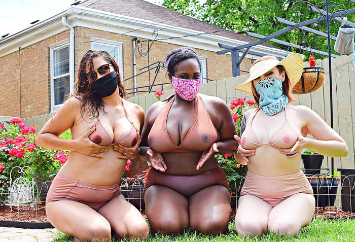 Three women kneel on a lawn wearing bikinis designed to look like breasts with nipples