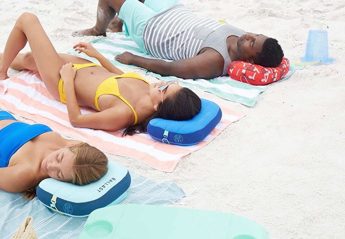 Three people lying out on the beach with the inflatable pillow