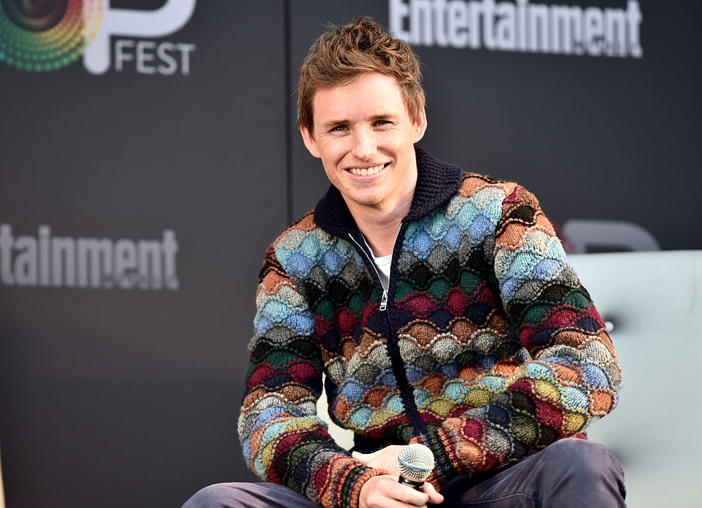 Eddie Redmayne smiling with a mic in his hand at an event