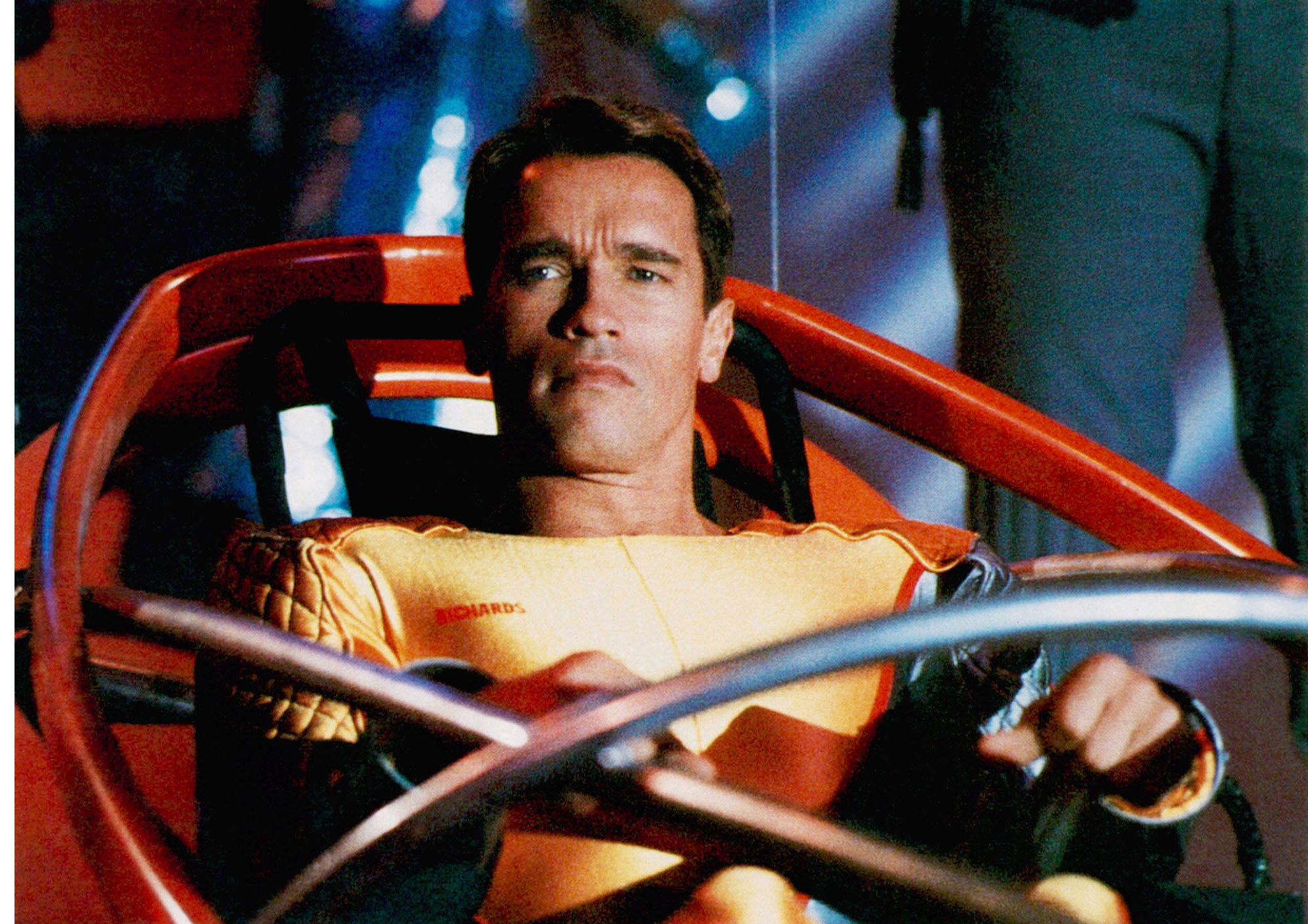 A man in an orange jumpsuit sits in a futuristic vehicle