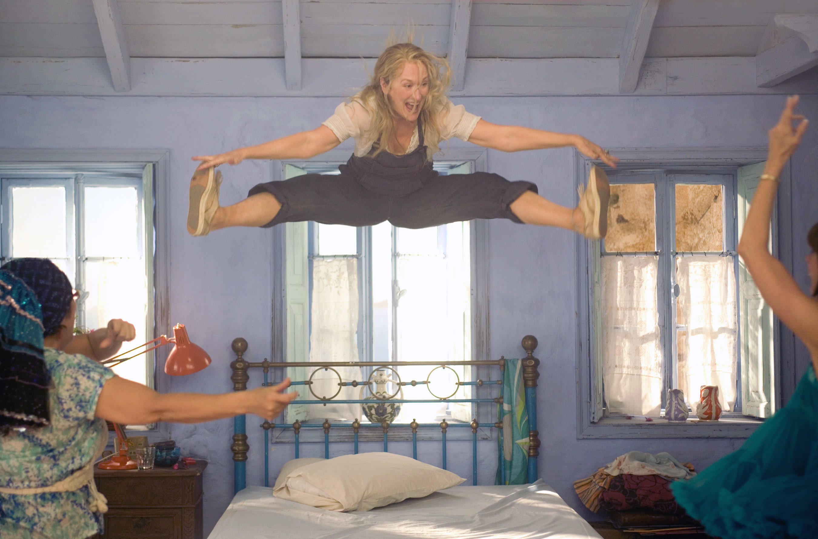 A woman jumps and dances playfully on a bed