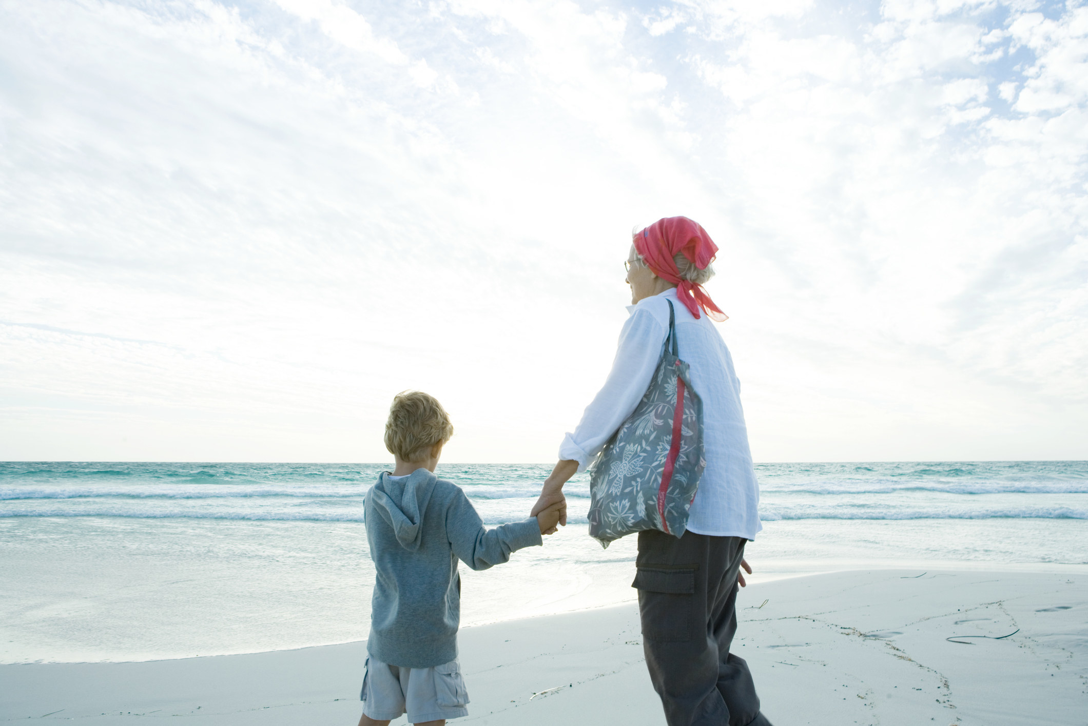 A child holds hands with his grandmother on the beach
