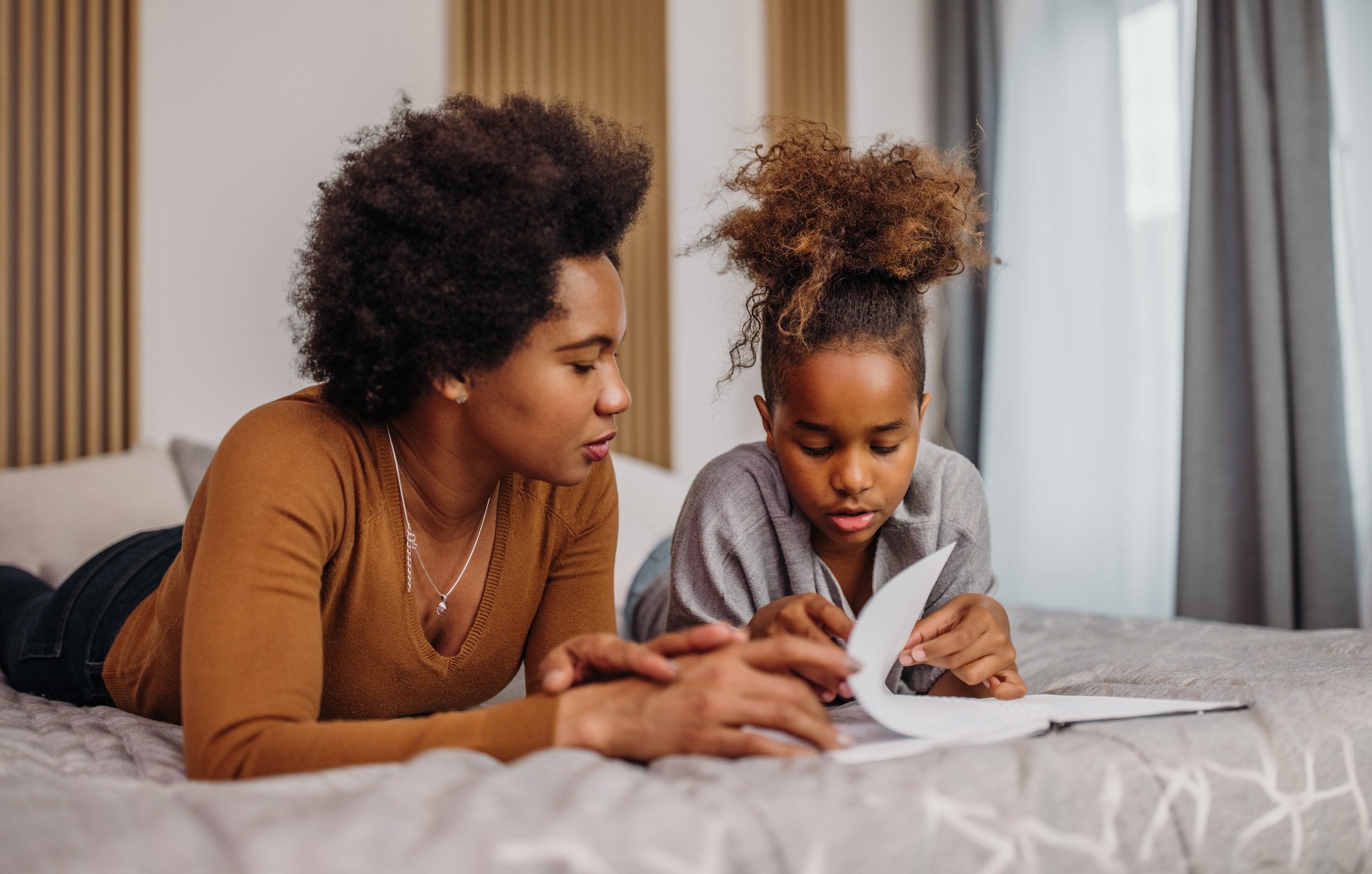 mother and daughter lying on bed reading a book