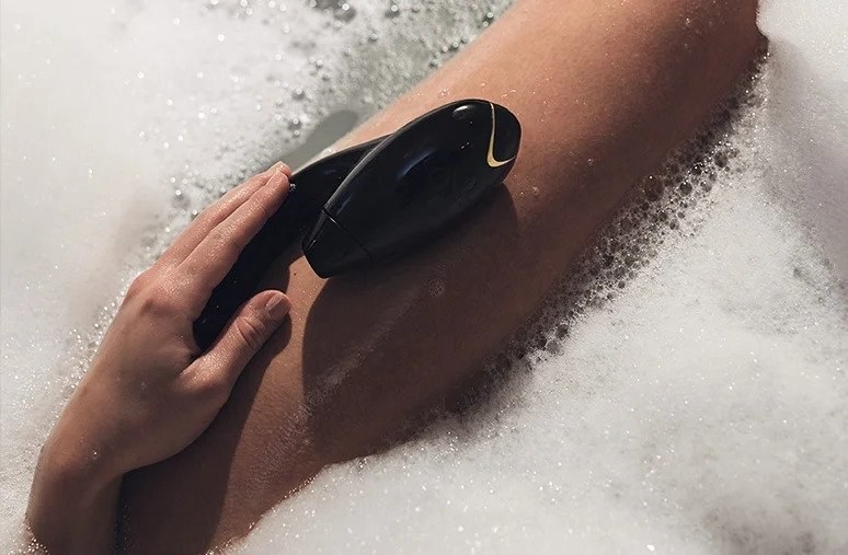 Model holding black dual-stimulating vibrator in bath