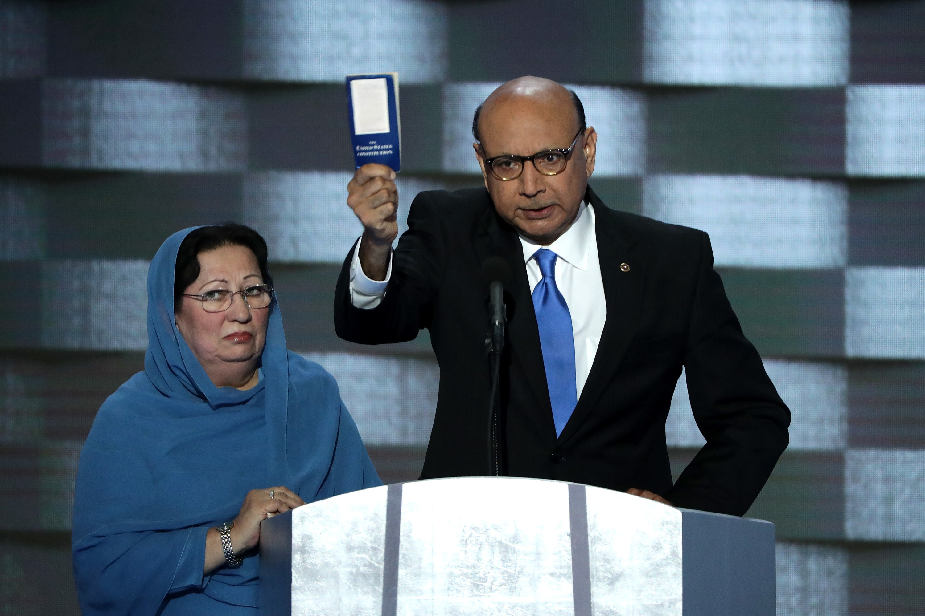 Khizr Khan is shown holding up a copy of the constitution as he gives a speech next to his wife at the 2016 DNC