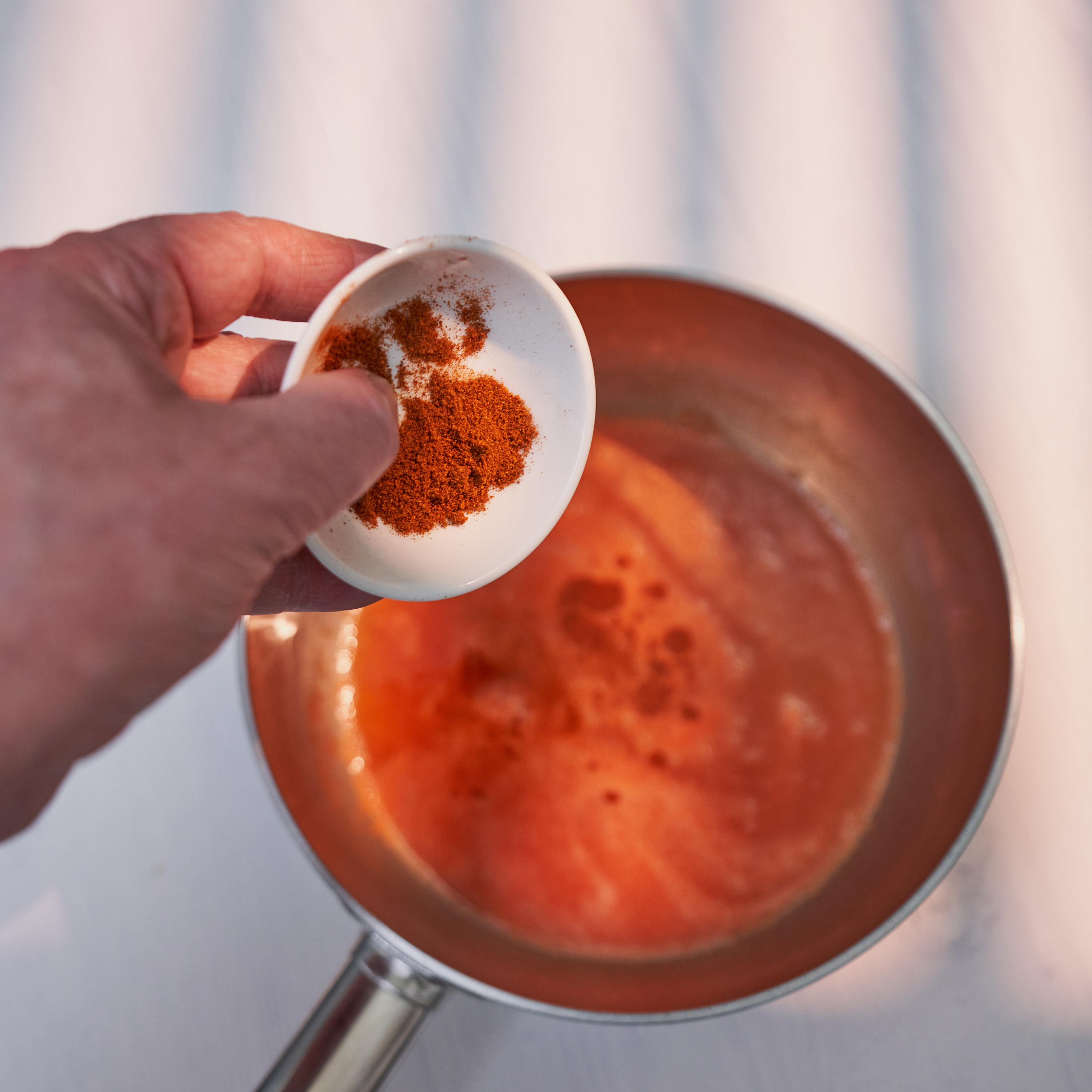 a hand holding a small bowl of cayenne above a pot