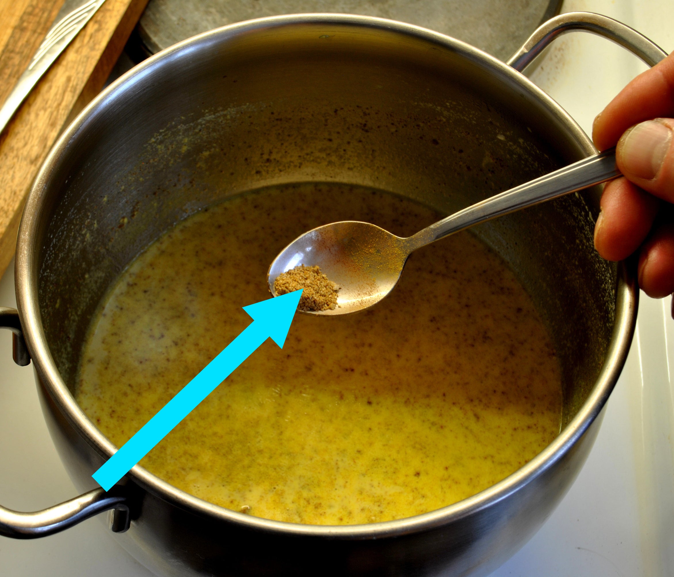 ground cardamom in a spoon being held above a pot