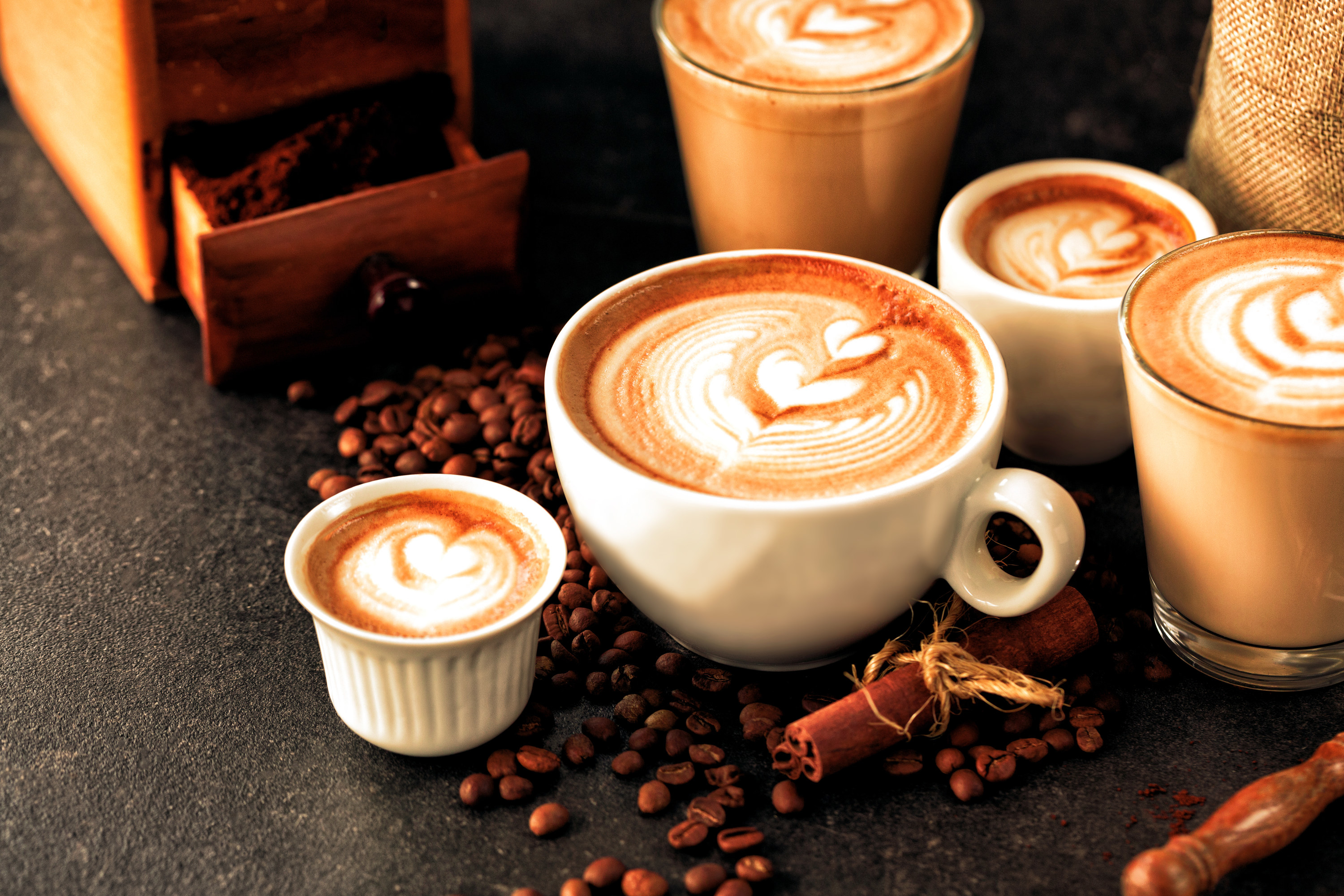 five lattes on a counter decorated with coffee beans and cinnamon sticks