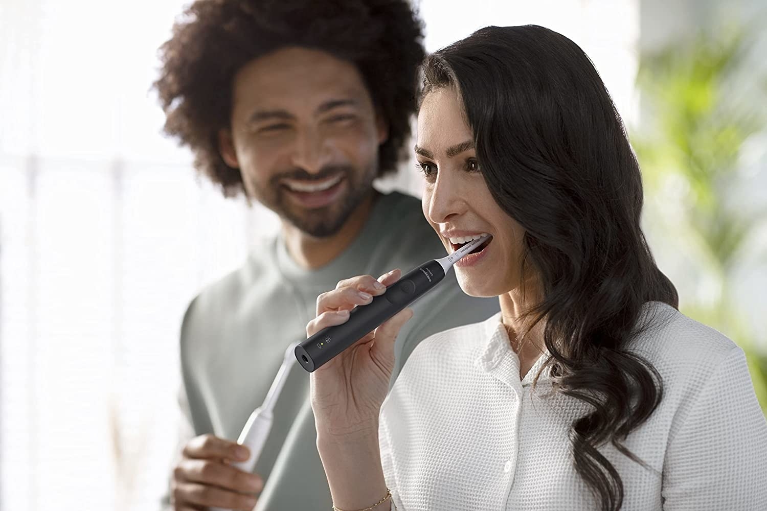 a couple both using the electric toothbrushes to clean their teeth