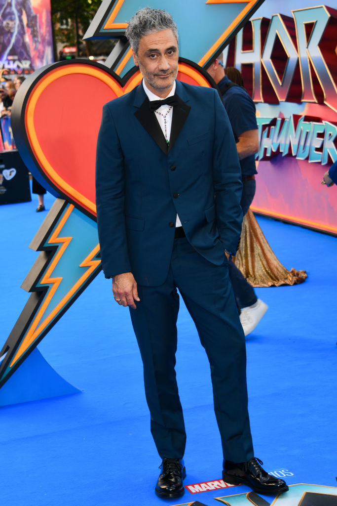 with one hand in the pocket of his colorful suit, Taika smiles for the red carpet camera