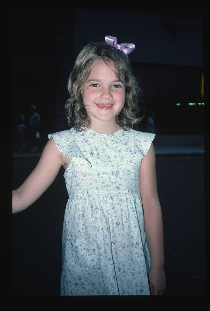 Drew as a young girl wearing a bow in her hair and a sleeveless floral-print dress