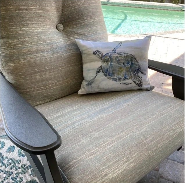 A green and blue and purple water color turtle pillow on tan seat outside a reviewer&#x27;s home