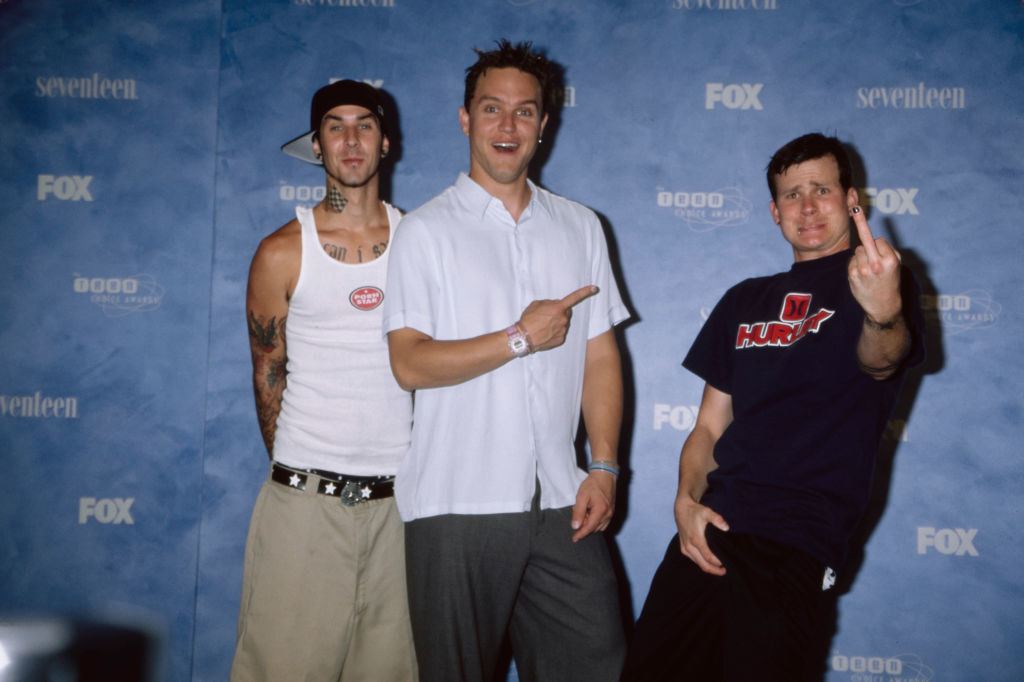 Travis is with other members of Blink-182 and wearing an undershirt and baggy pants