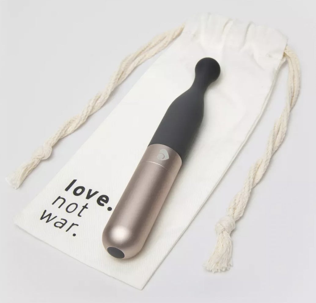 The sleek clitoral stimulator wand resting atop bamboo storage bag that reads love. not war