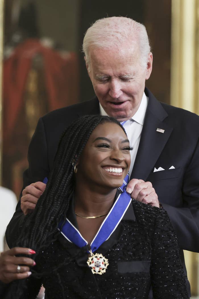 Simone grinning widely while Joe Biden puts the Medal of Freedom around her neck