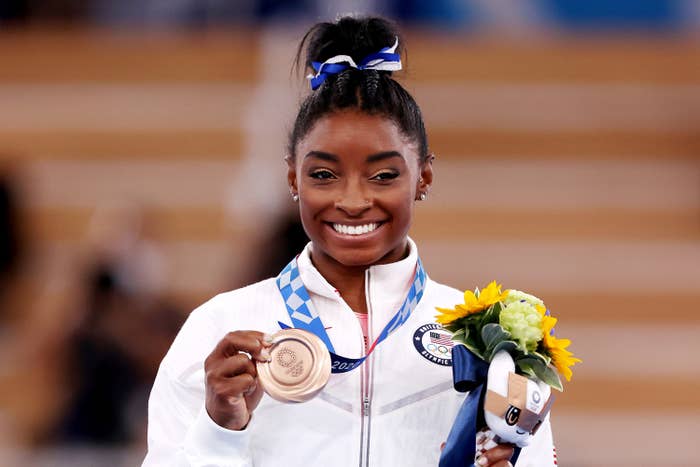 Simone smiling and holding up her medal during a medal ceremony