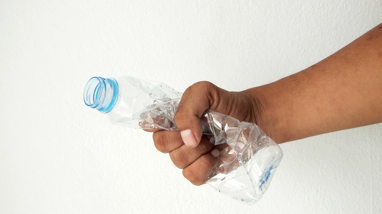 a hand crumpling up a plastic water bottle
