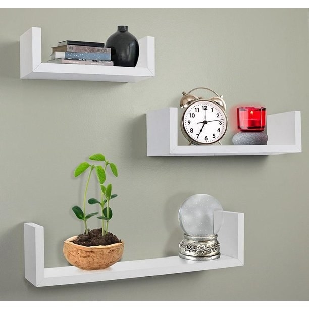 three white floating shelves holding a plant, clock, and orb