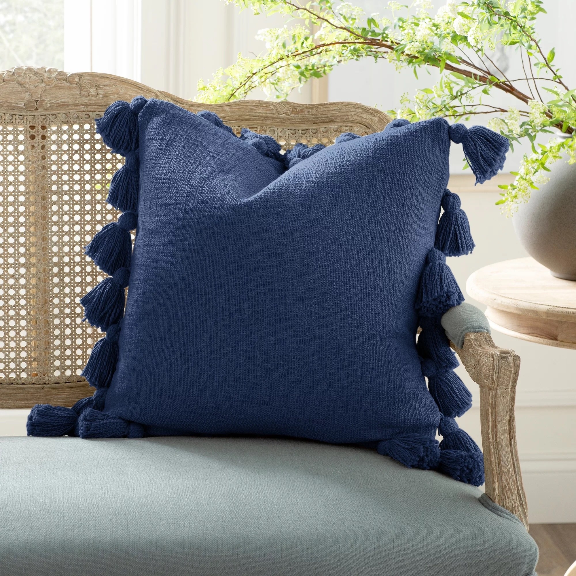 a navy blue pillow cover and insert with tassels laying on a chair