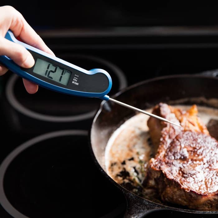 thermometer testing the temperature of steak on a skillet
