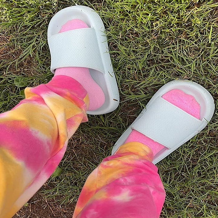 reviewer wearing the light blue slippers with pink socks and tie-dye pants