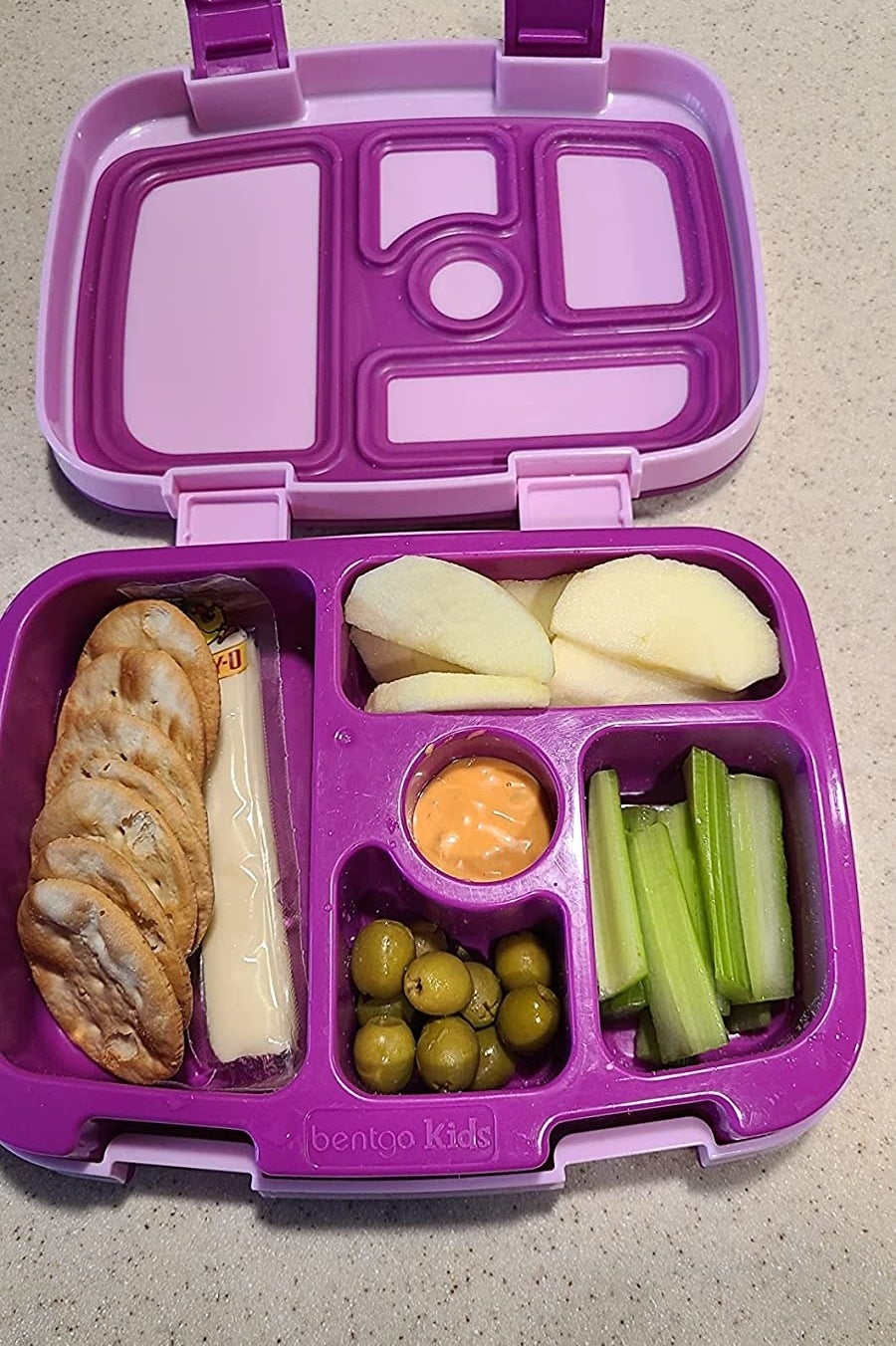 a reviewer&#x27;s purple lunch box packed with olives, celery, apple slices, crackers, and cheese
