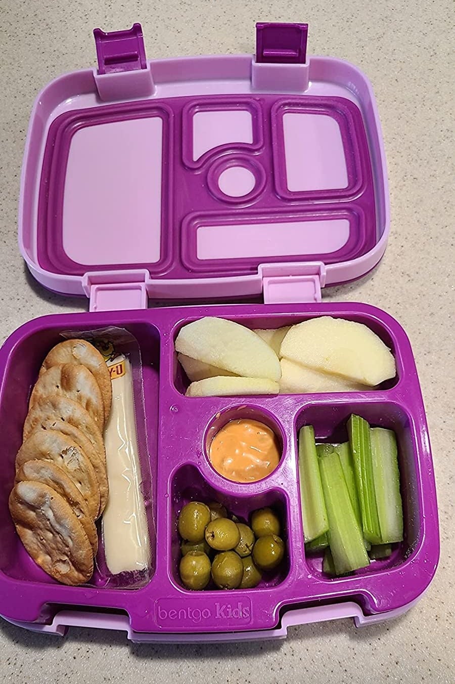 a reviewer&#x27;s purple lunch box packed with olives, celery, apple slices, crackers, and cheese