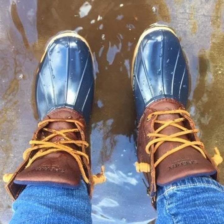 reviewer wearing the blue and brown boots while standing in a puddle