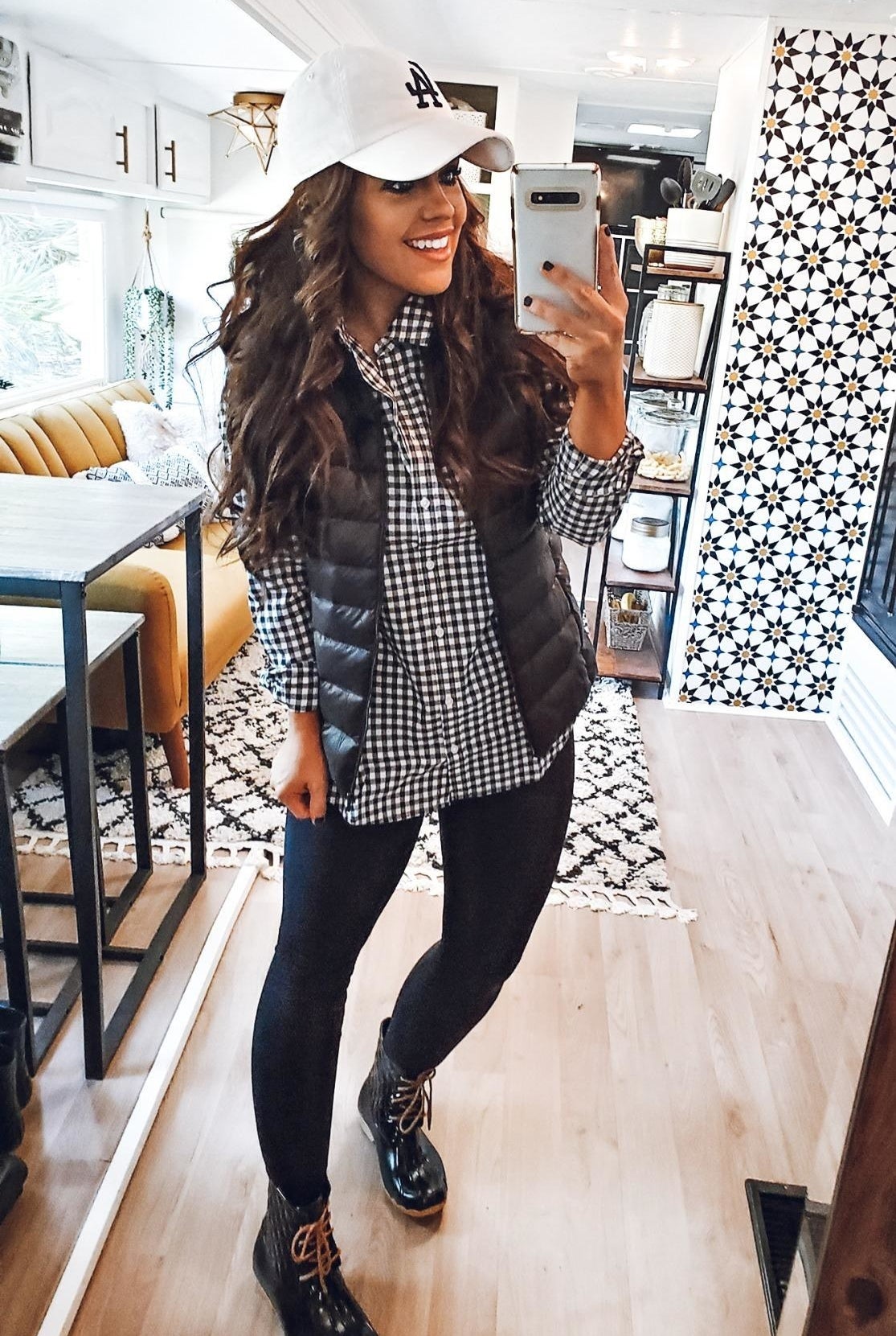 reviewer wearing the black and white checkered shirt under a black vest with black leggings and ankle boots