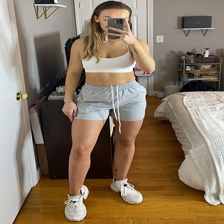 reviewer wearing the gray shorts with a white sports bra and sneakers