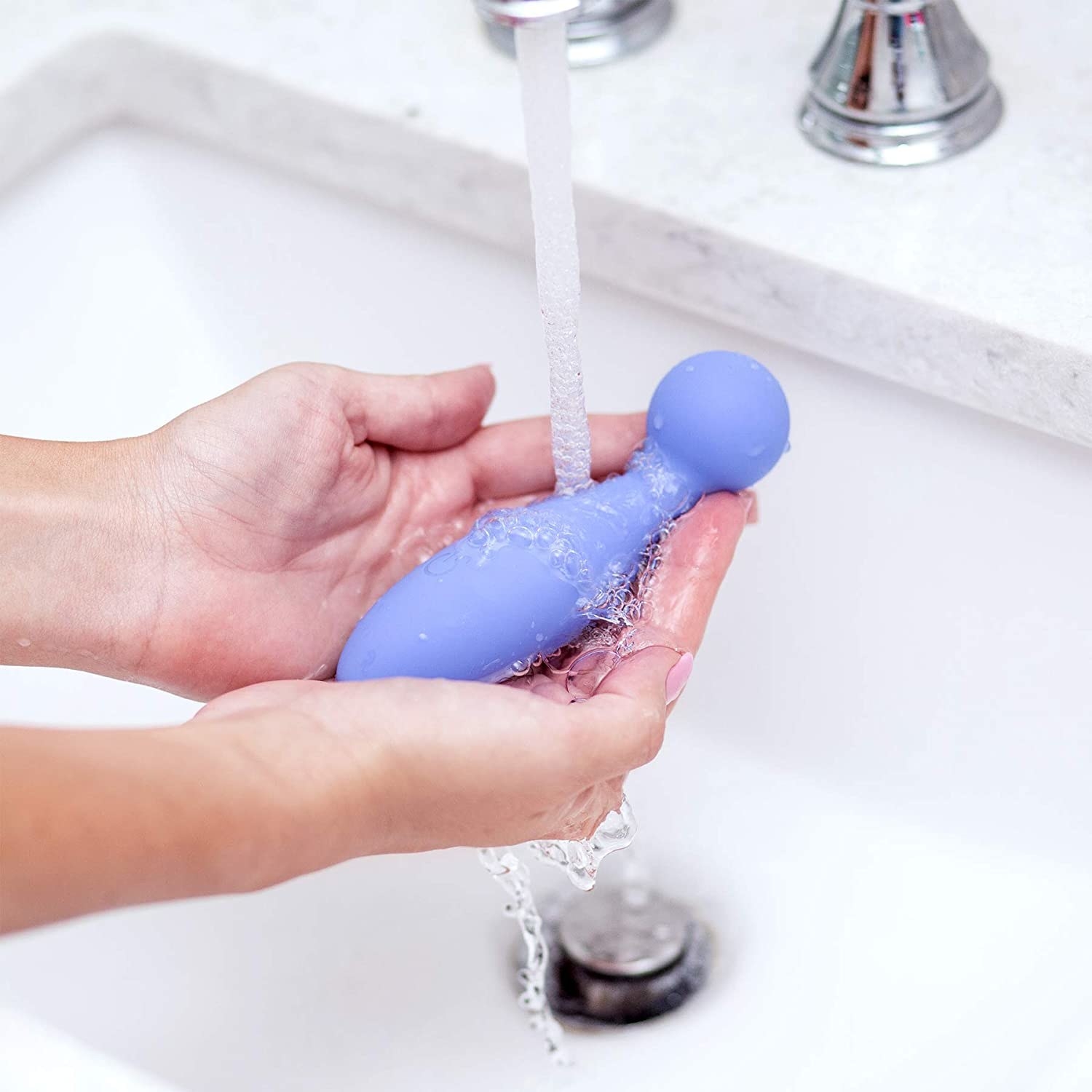 Hands holding periwinkle vibrator under running faucet