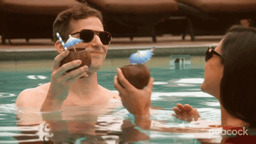 Jake and Amy saying cheers with coconut cups in a pool from an episode of brooklyn 99