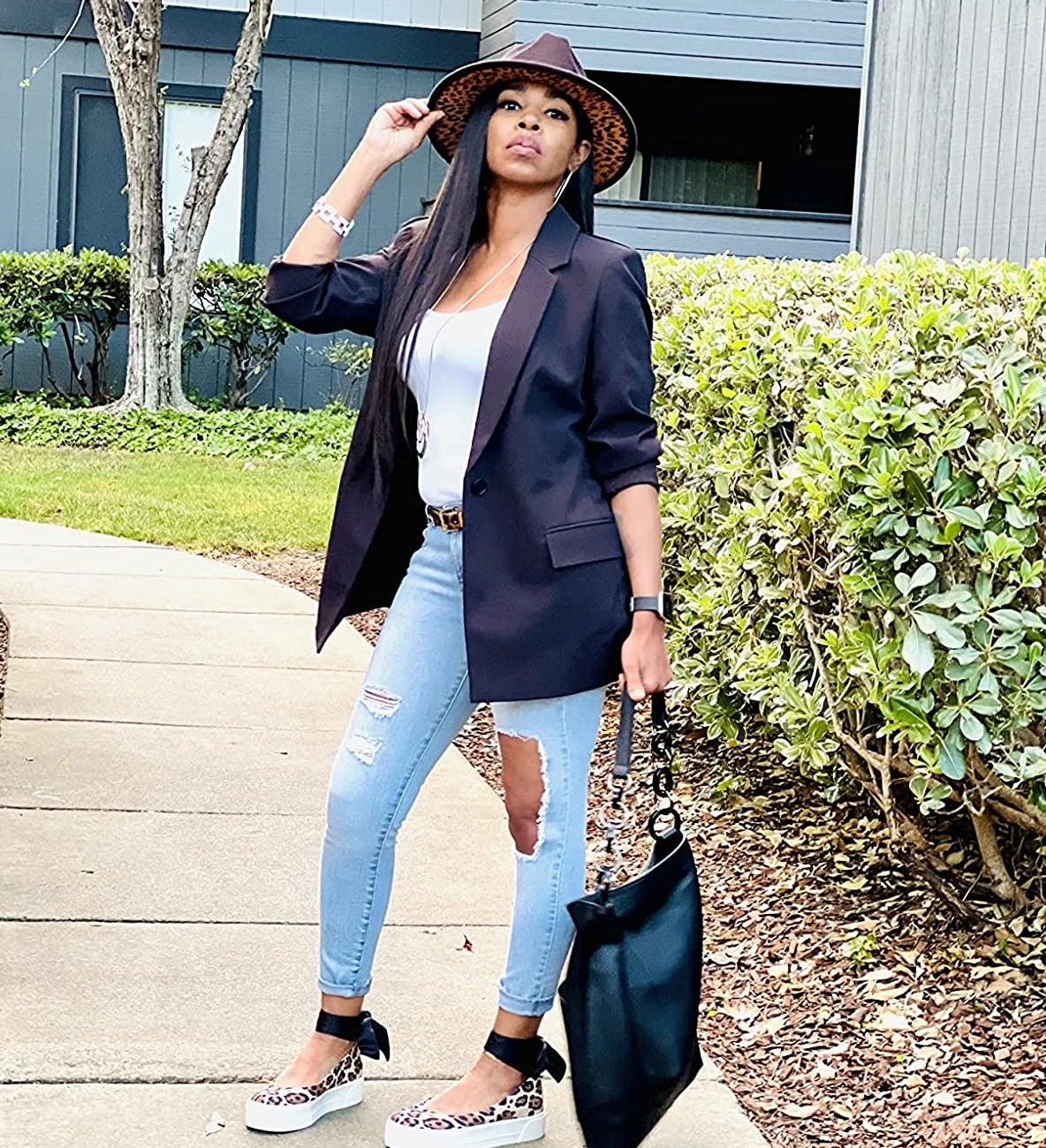 Reviewer wearing the black blazer over white tank and jeans with cheetah print wedge sandals and wide brimmed hat