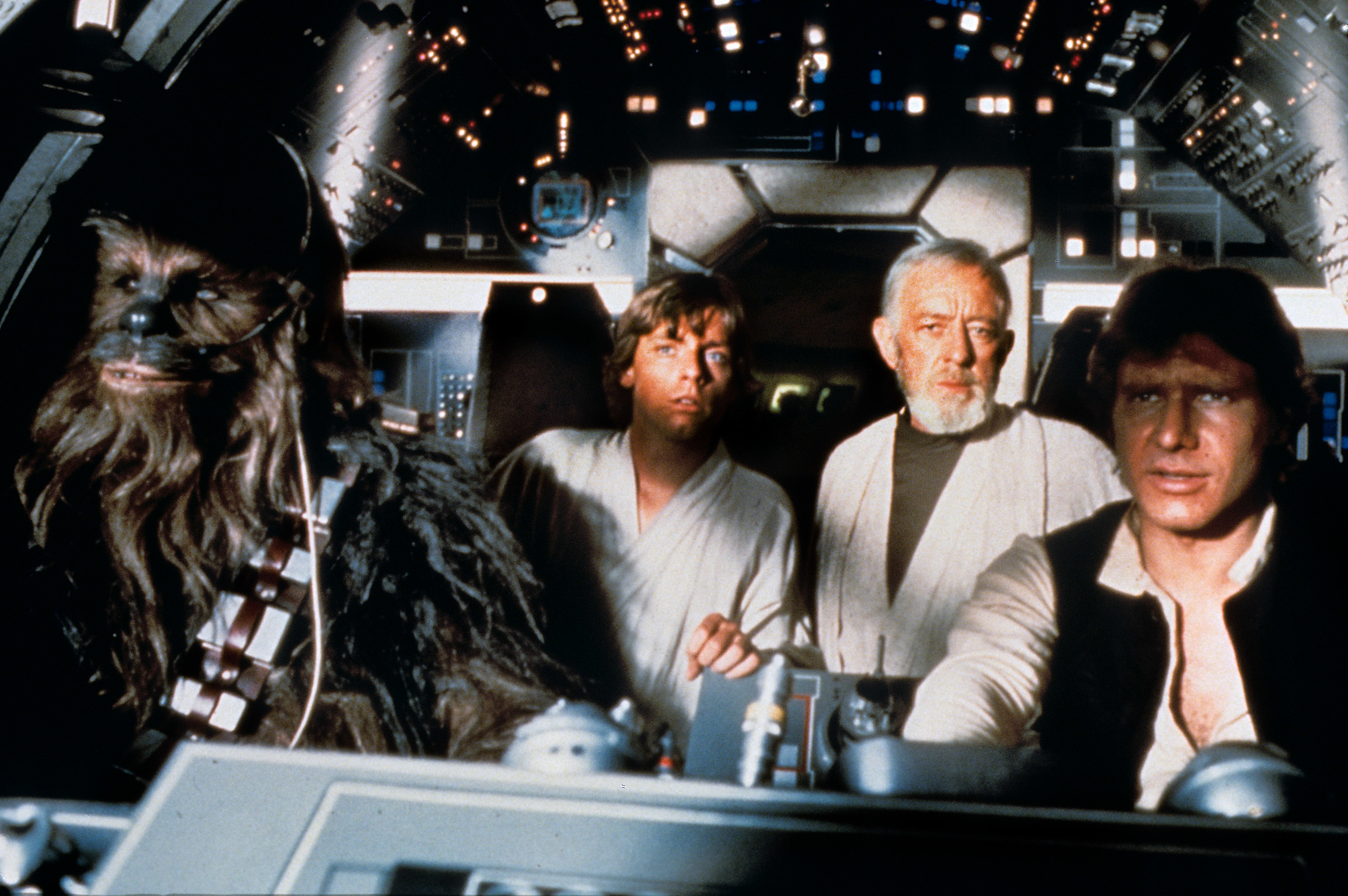 A wookie and three men in the cockpit of the Millennium Falcon