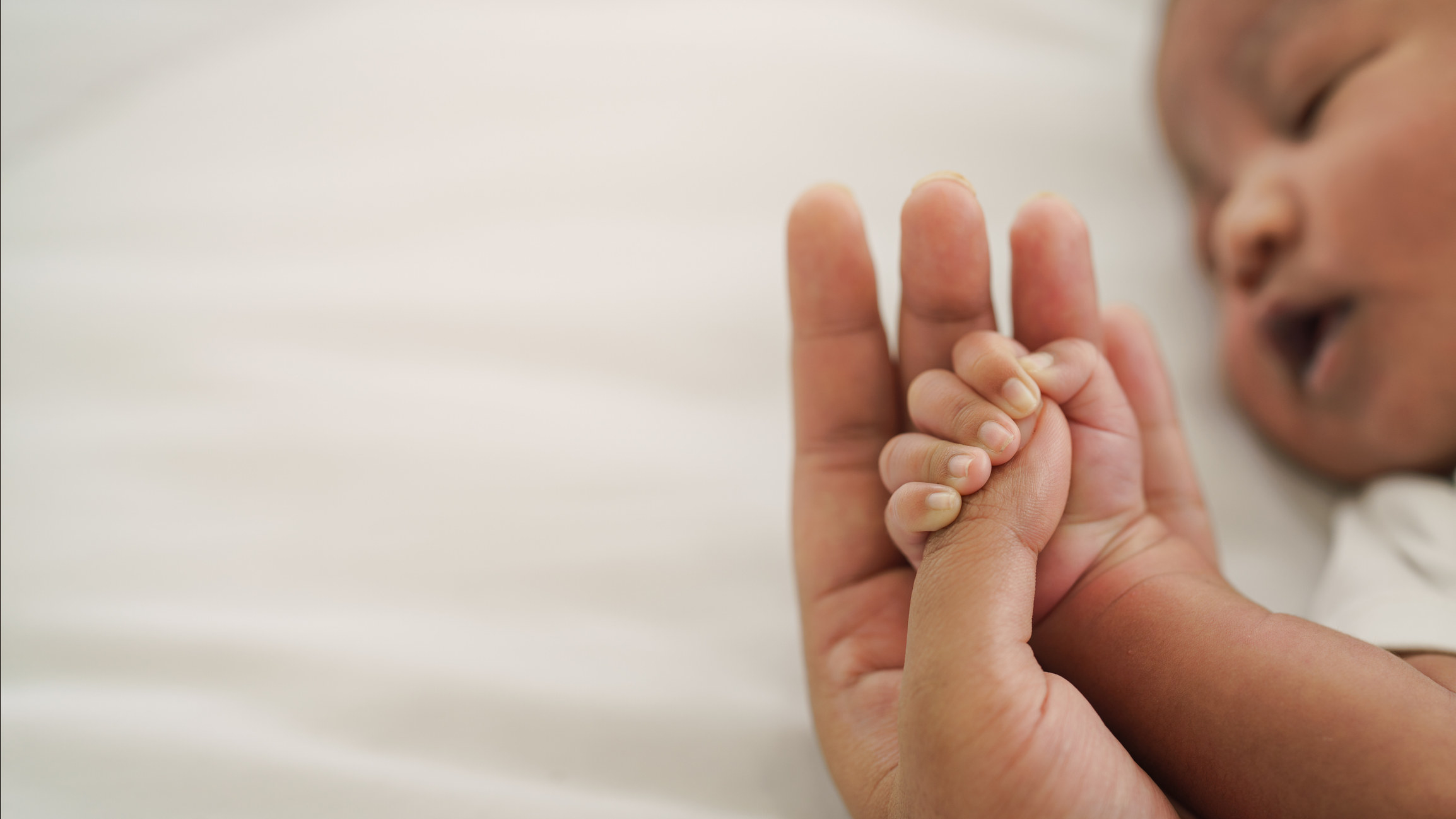 A parent holding a newborn&#x27;s hand.