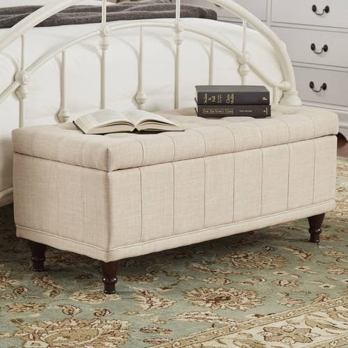 Beige tufted storage bench at the foot of bed with one open book and two stacked books on top