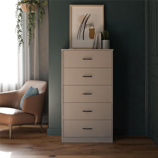 light gray tall dresser on wooden floor with picture frame above it, books and vase on top of dresser