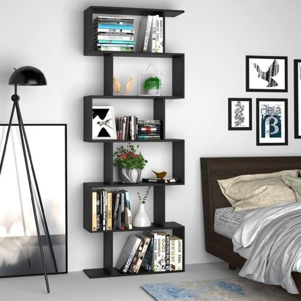 Black geometric book case against wall with books and various decorative objects in open cubbies, next to bed