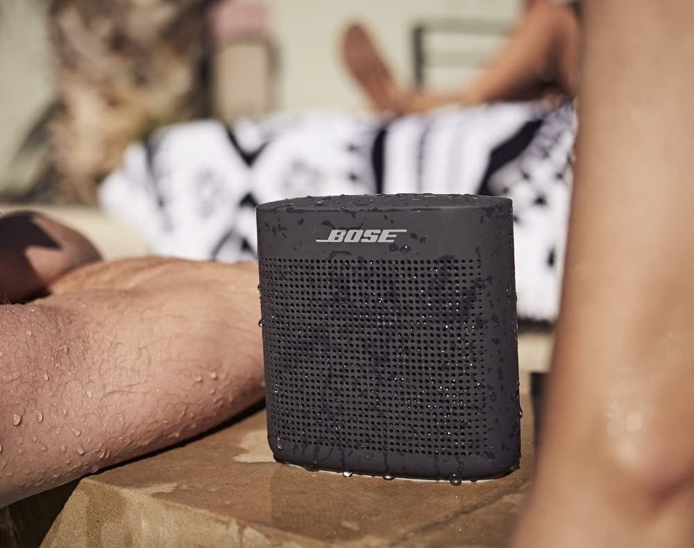 the black speaker sat beside a pool having been splashed on